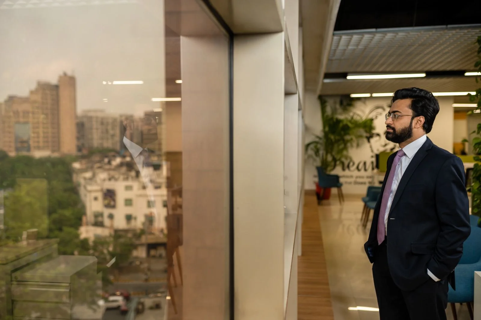 Abhishek Chaudhary in a dark suit, looking out of an office window over the city